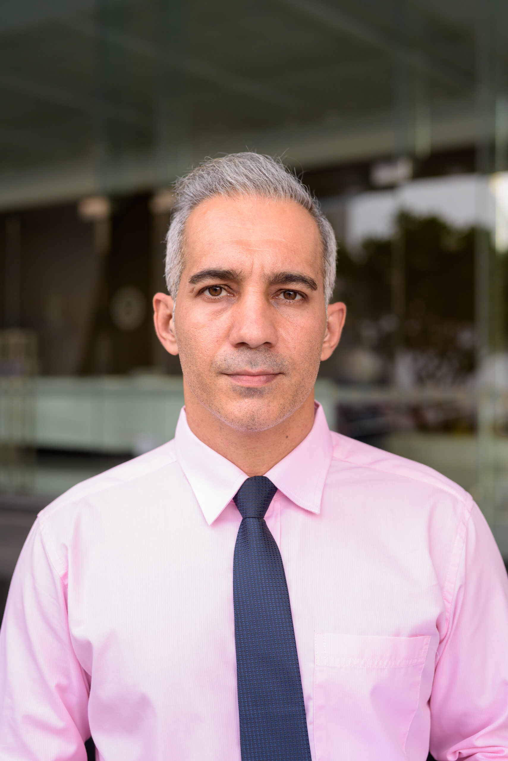 Portrait of handsome Persian businessman with gray hair outside modern building in the city